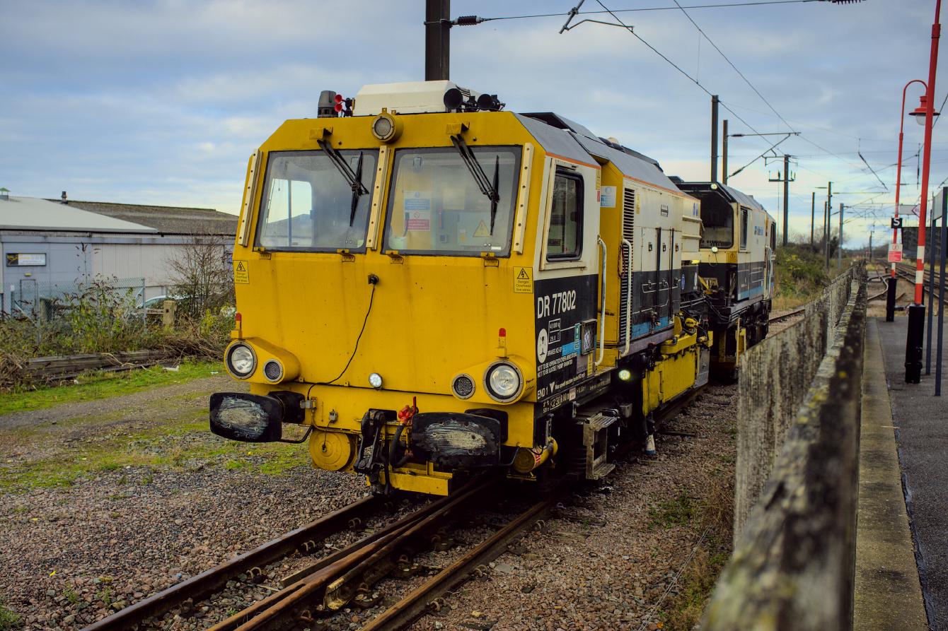DR 77802, a track tamping machine, sitting in the siding at Downham Market. It is about the size of a large locomotive and is self-propelled, with a cab on either end.