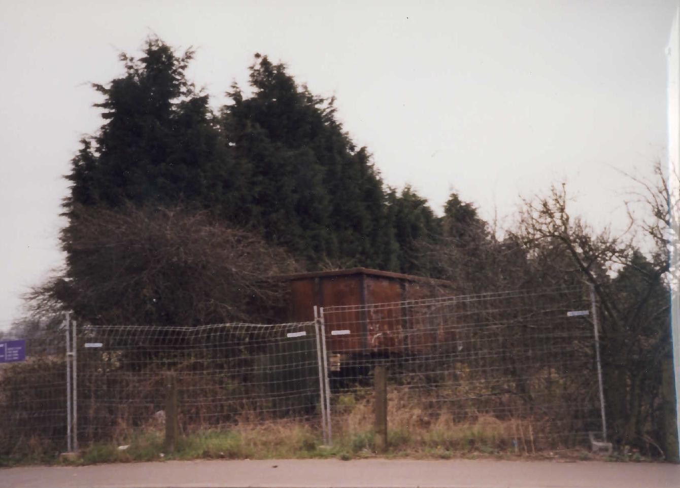B558090, a small wagon for transporting coal. It sits here in its abandoned state; it is surrounded by vegetation with some clearly growing inside it. It sits behind security fencing.