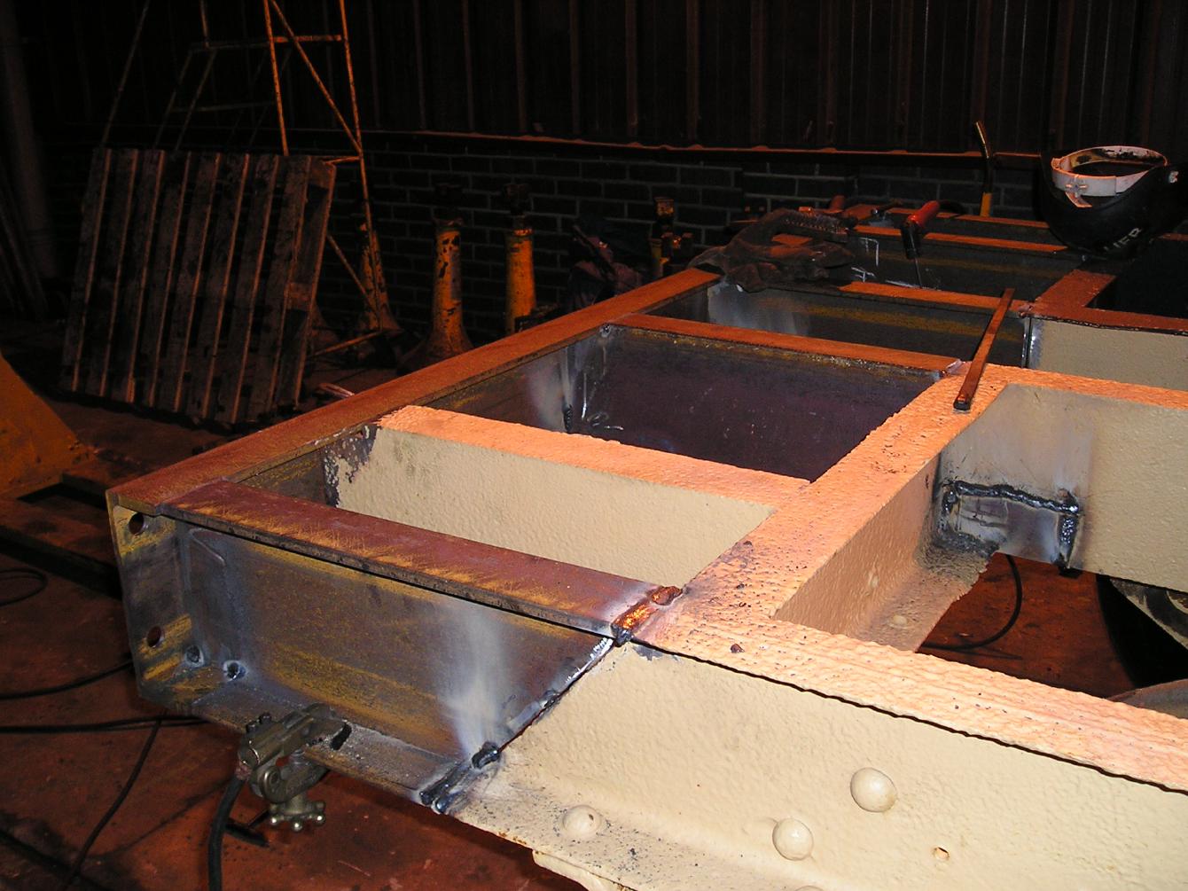 The chassis of B558090 undergoing repair; a substantial chunk has been cut out of it with new, shiny chunks welded into place.