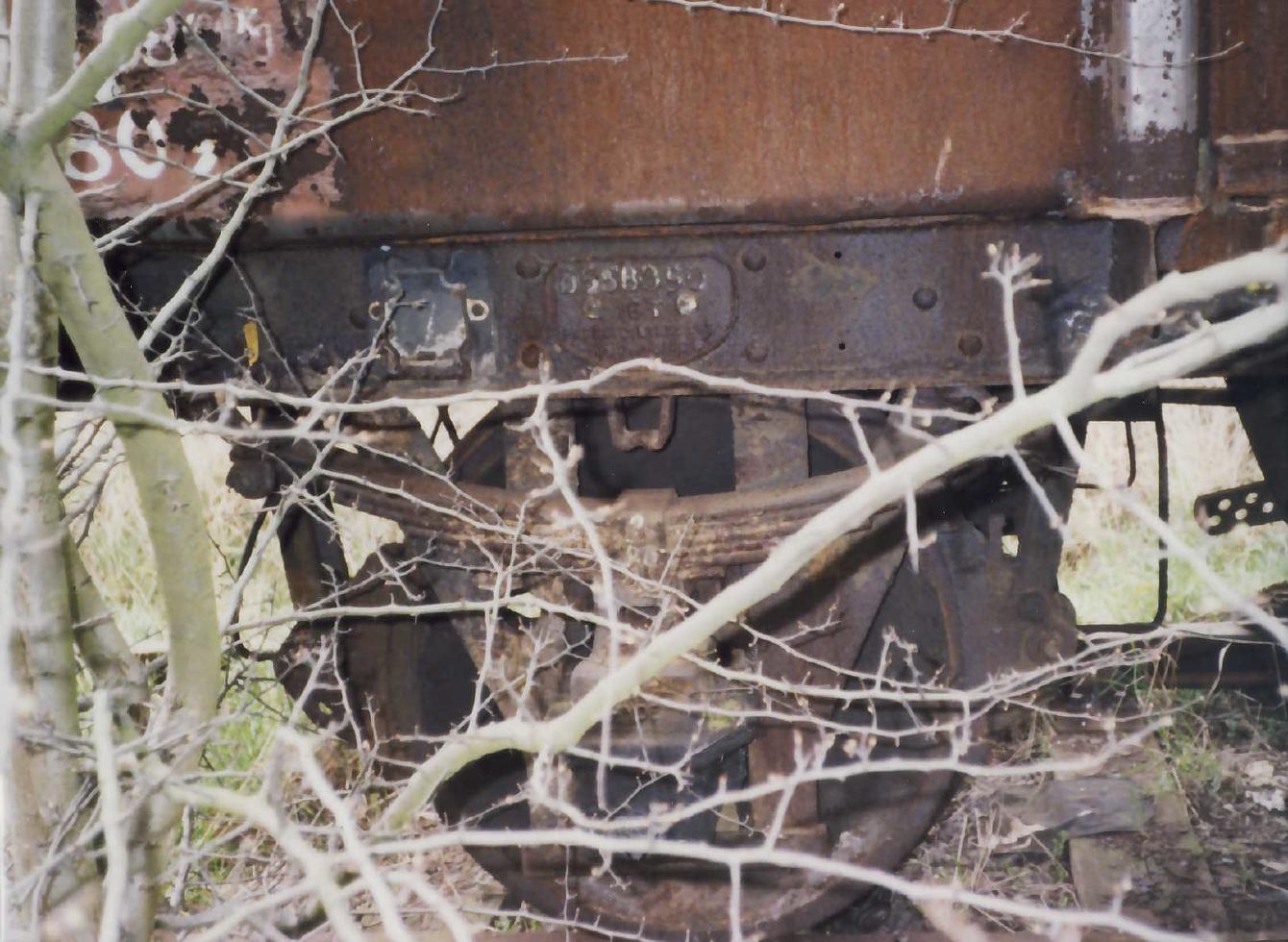 A close-up of the axle box and springs of B558090, showing its number plate. More vegetation is visible in the foreground.
