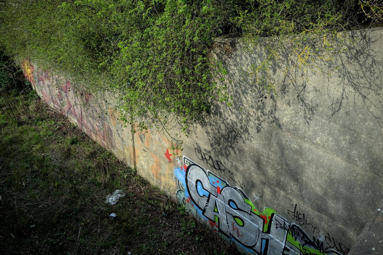 Looking down from the deck of a bridge, the wing walls of a single-track concrete bridge over a single-track railway.