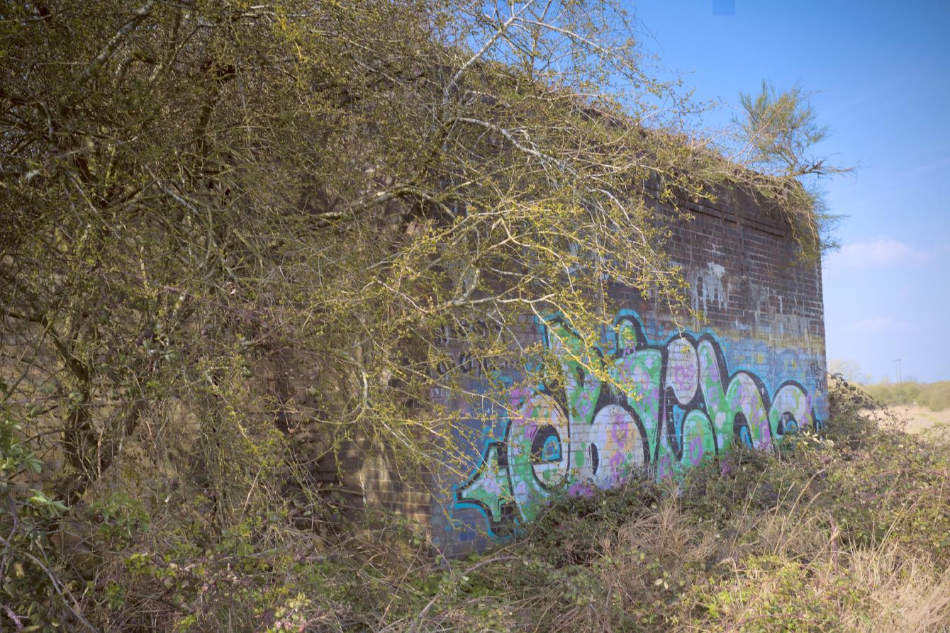 A brick bridge abutment; some overgrowth peeks out at the top, and graffiti covers the bottom half of it.