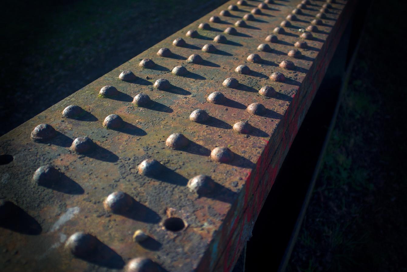 A close up of the domed tops of some hot rivets in one of the girders of SOL/51. Strong sun casts long shadows on each one.