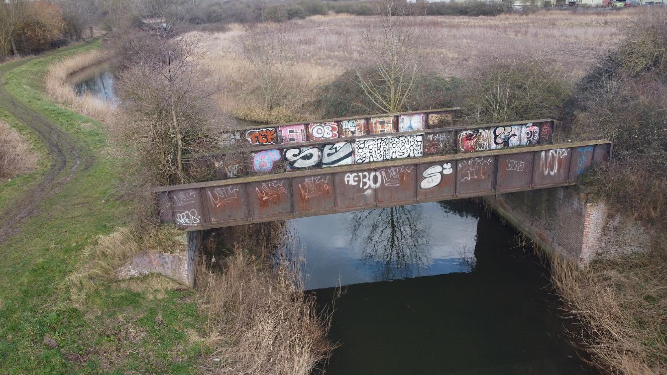 An aerial view of the bridge, showing the deck, and space for two separated tracks, and vegetation growing especially on the east bank.