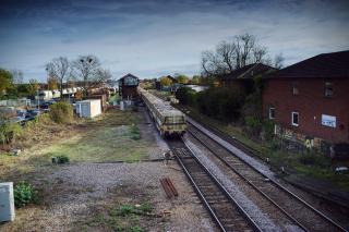 A view from the footbridge of March station, looking away from the platforms eastwards. The signal box is visible, as is a small marshalling yard on the left. The rear of a ballast train heading east is visible.