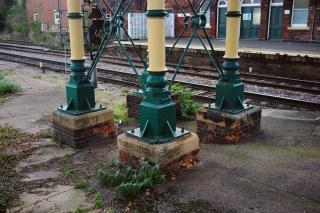 More detail of the footbridge at March station. We are looking at a set of four pillars that supports it. They are made of iron, painted in cream and green, and sitting on brick-and-concrete pads.