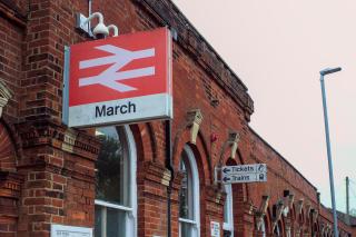 Two signs in the standard British Rail style at March railway station, outside. One has a double arrow in white-on-red and March written under it in black-on-white. A second pair of signs behind it shows directions for Tickets and Trains.