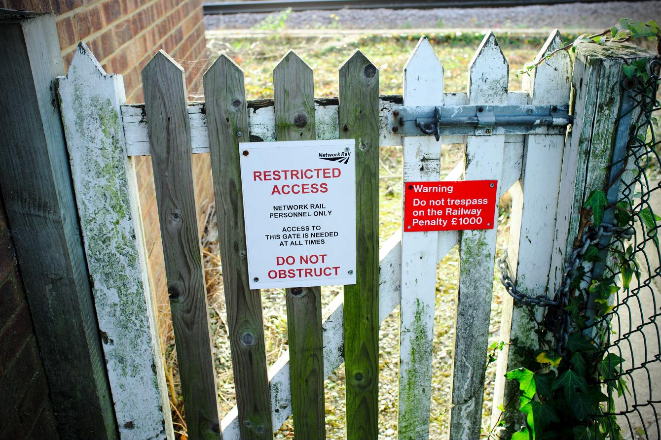 Two signs next to each other on a wooden gate. One says &ldquo;Network Rail/ RESTRICTED ACCESS / NETWORK RAIL PERSONNEL ONLY / ACCESS TO THIS GATE IS NEEDED AT ALL TIMES / DO NOT OBSTRUCT&rdquo; in several different type sizes. One says, in white-on-red text, &ldquo;Warning / Do not trespass on the railway / Penalty £1000.&rdquo;
