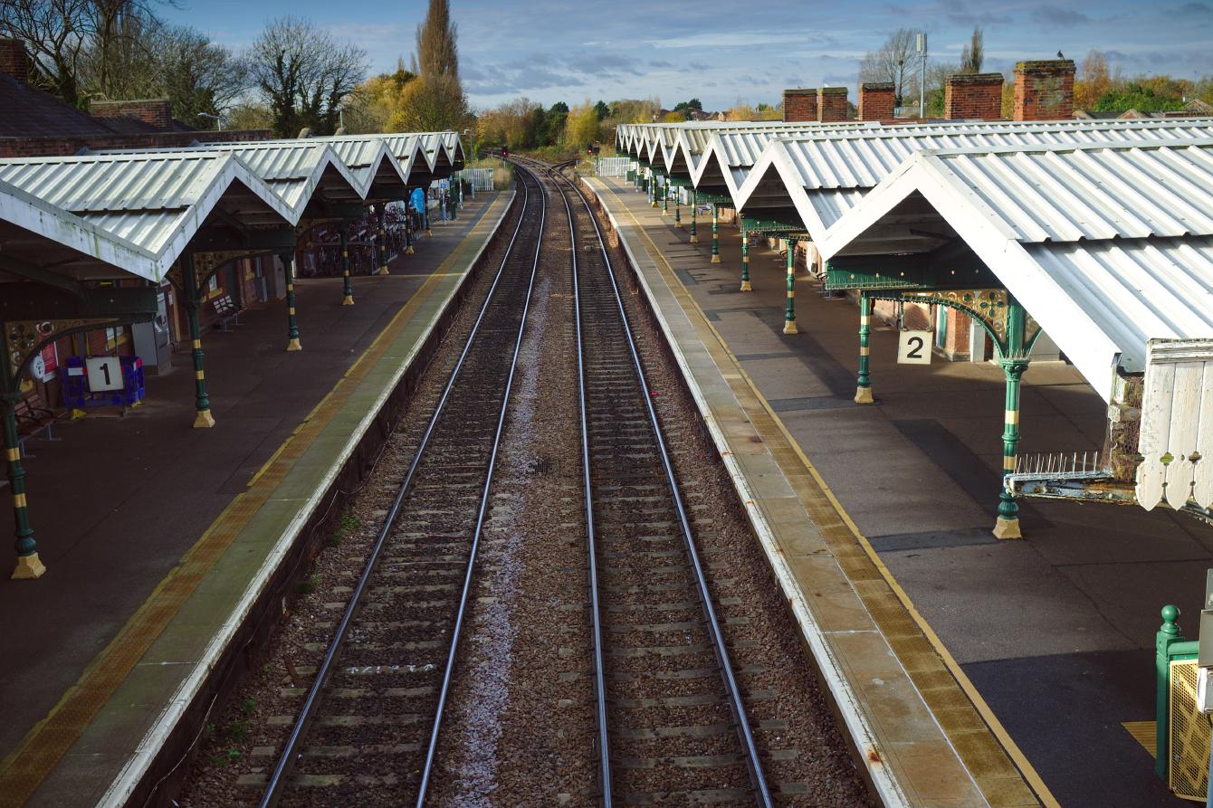 A view from the footbridge of March station, looking down at the tracks. The white canopy is made of multiple pent-roof sections; the triangles face outwards, such that a zig-zag pattern follows the line of the platform.
