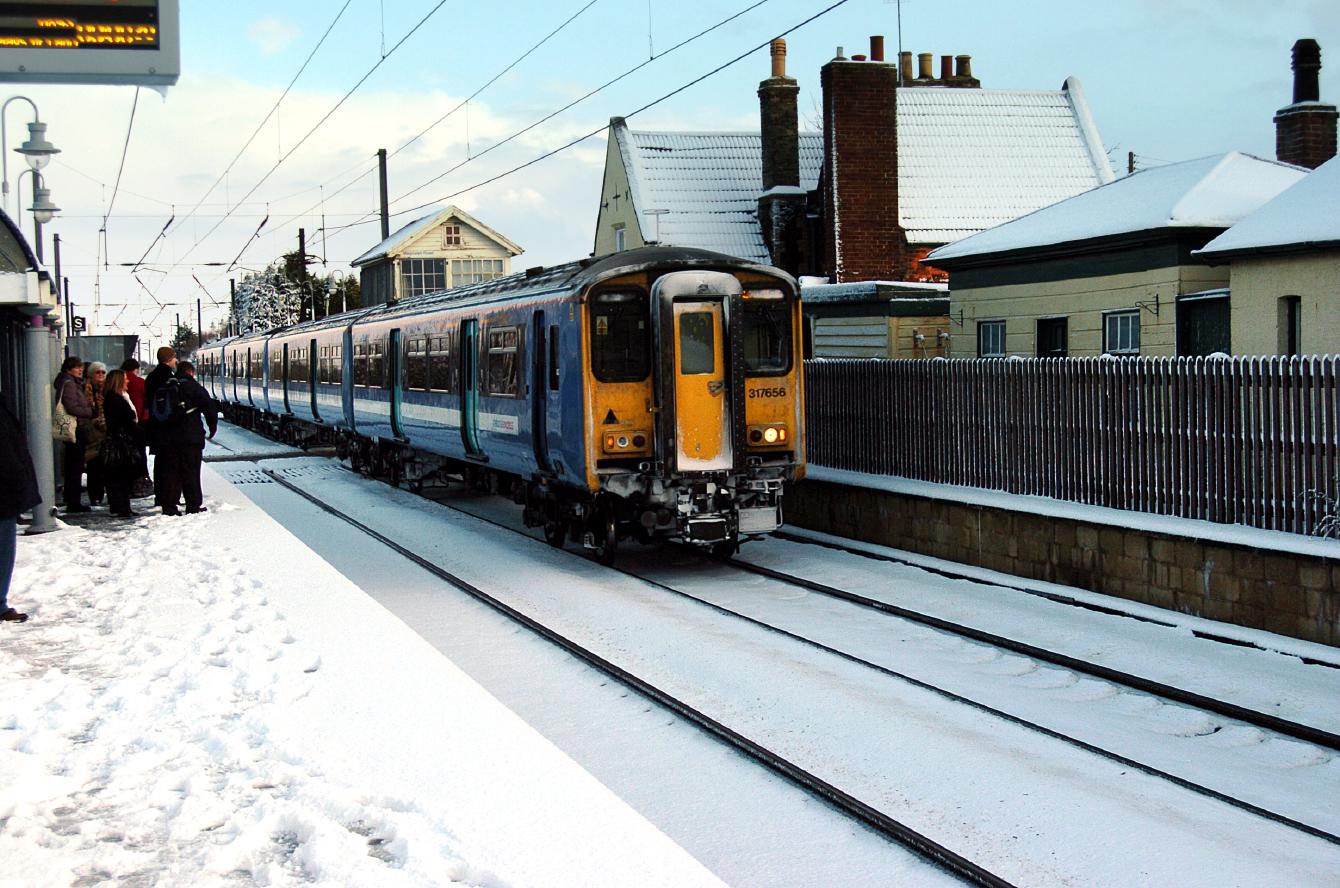 A Class 317 - a flat-fronted four-coach electric multiple unit - pulls out of a snowy Watlington station.