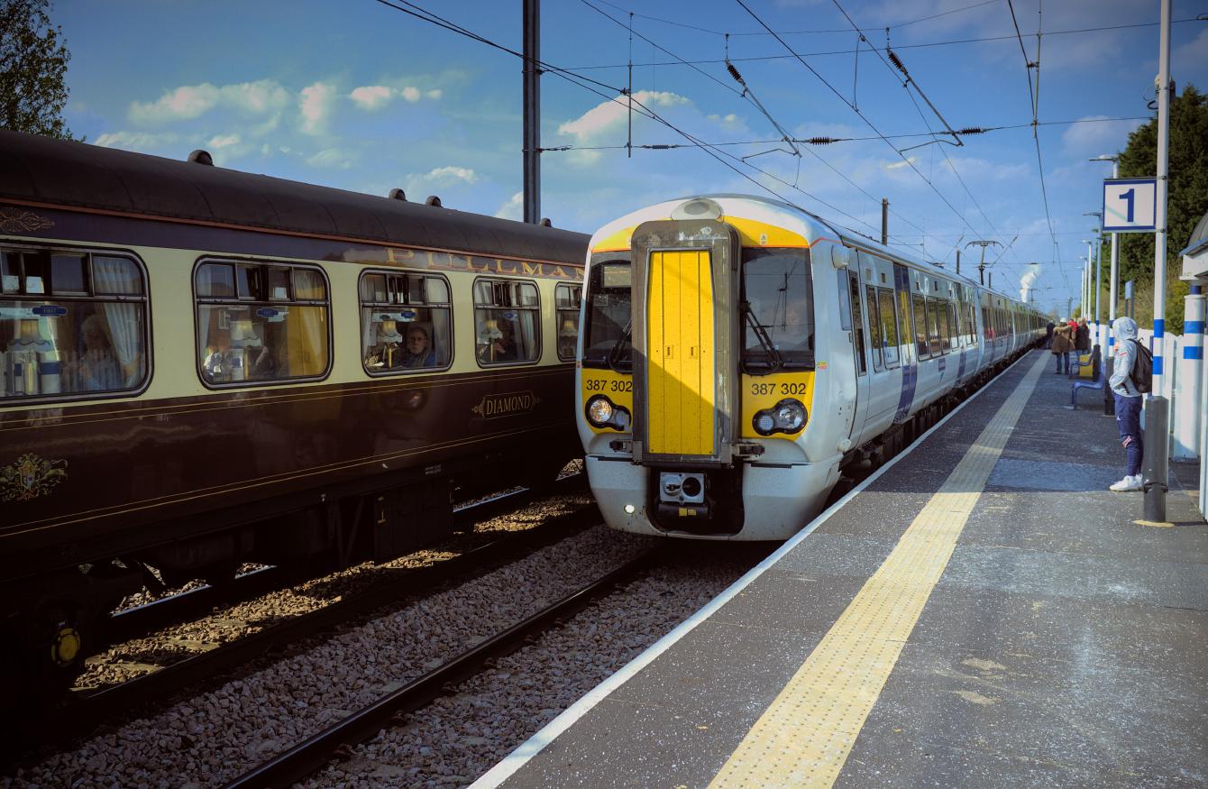 A modern white electric multiple unit in front of a brown-and-cream Pullman carriage on the other track.