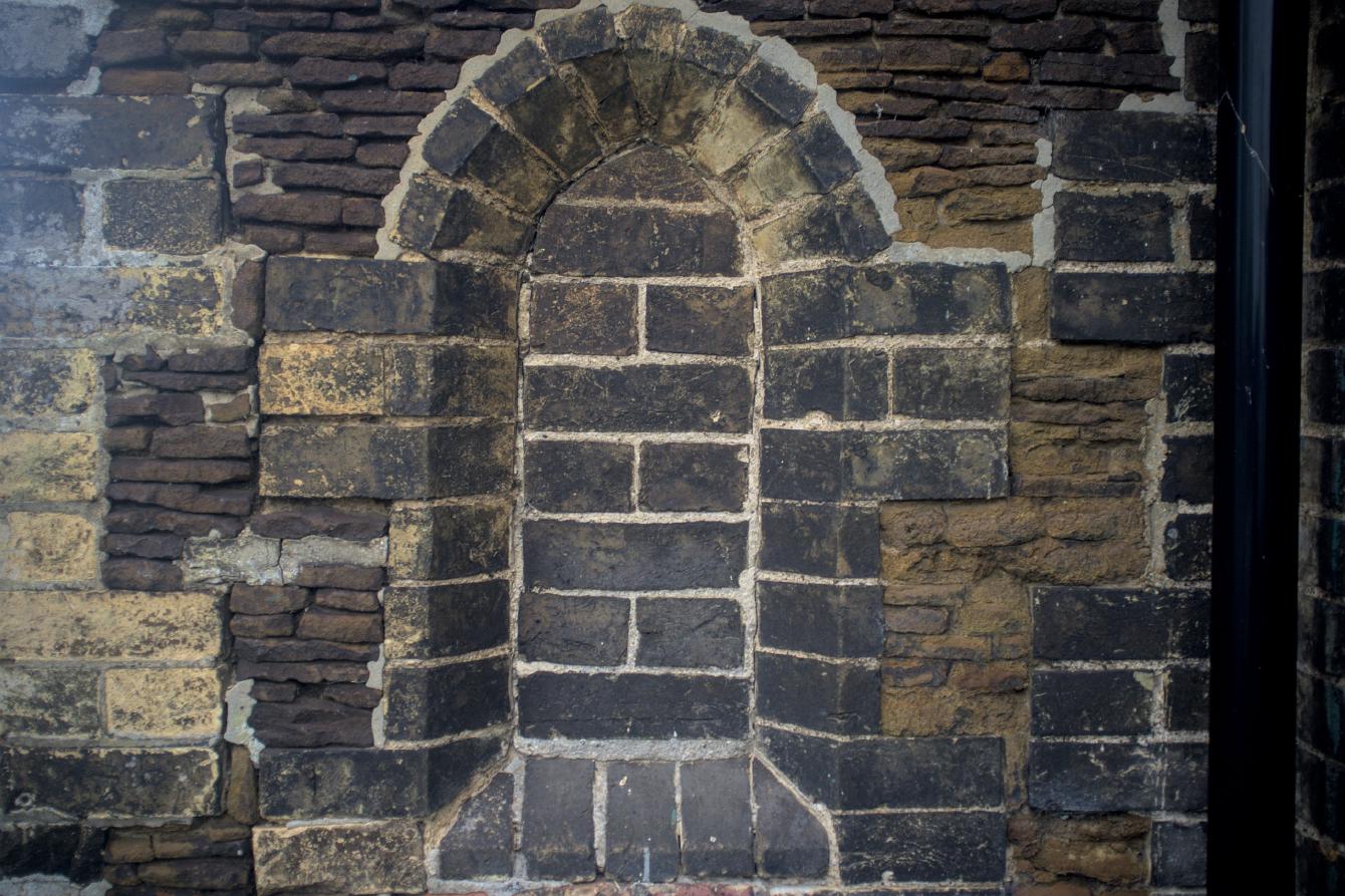 A tall arched window which has been bricked off.