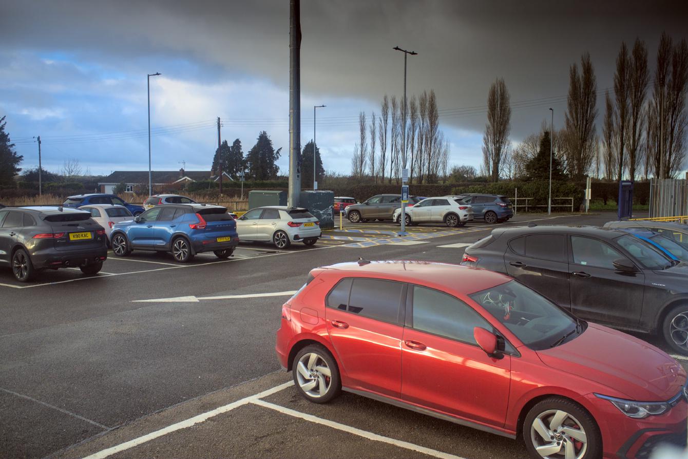 The tarmac car park at Watlington, about half-occupied; in the middle of it is a mobile phone mast.