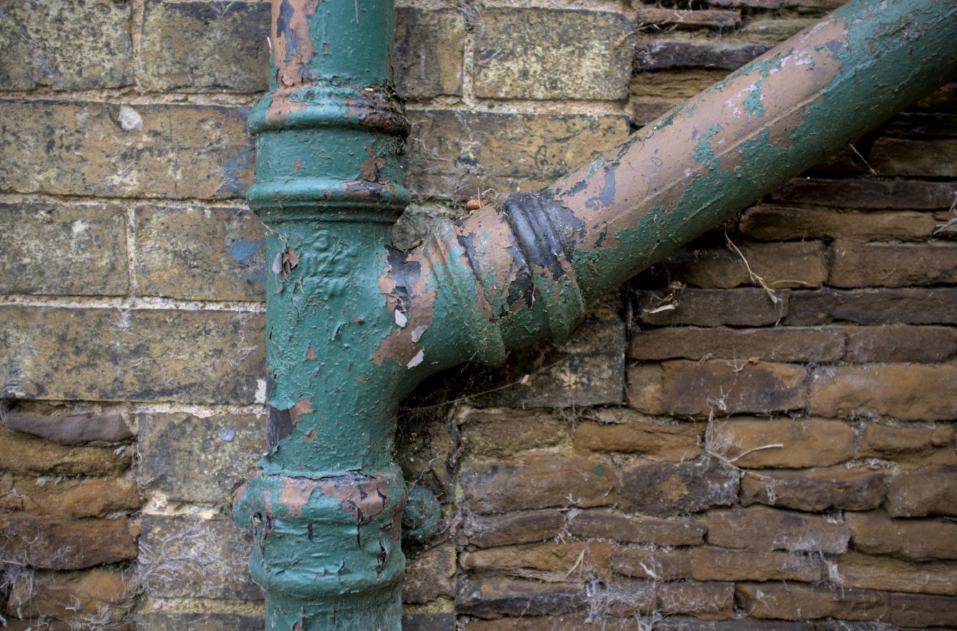 A close up of some old drain pipes; layers of paint flake off exposing what looks like clay pipework underneath.