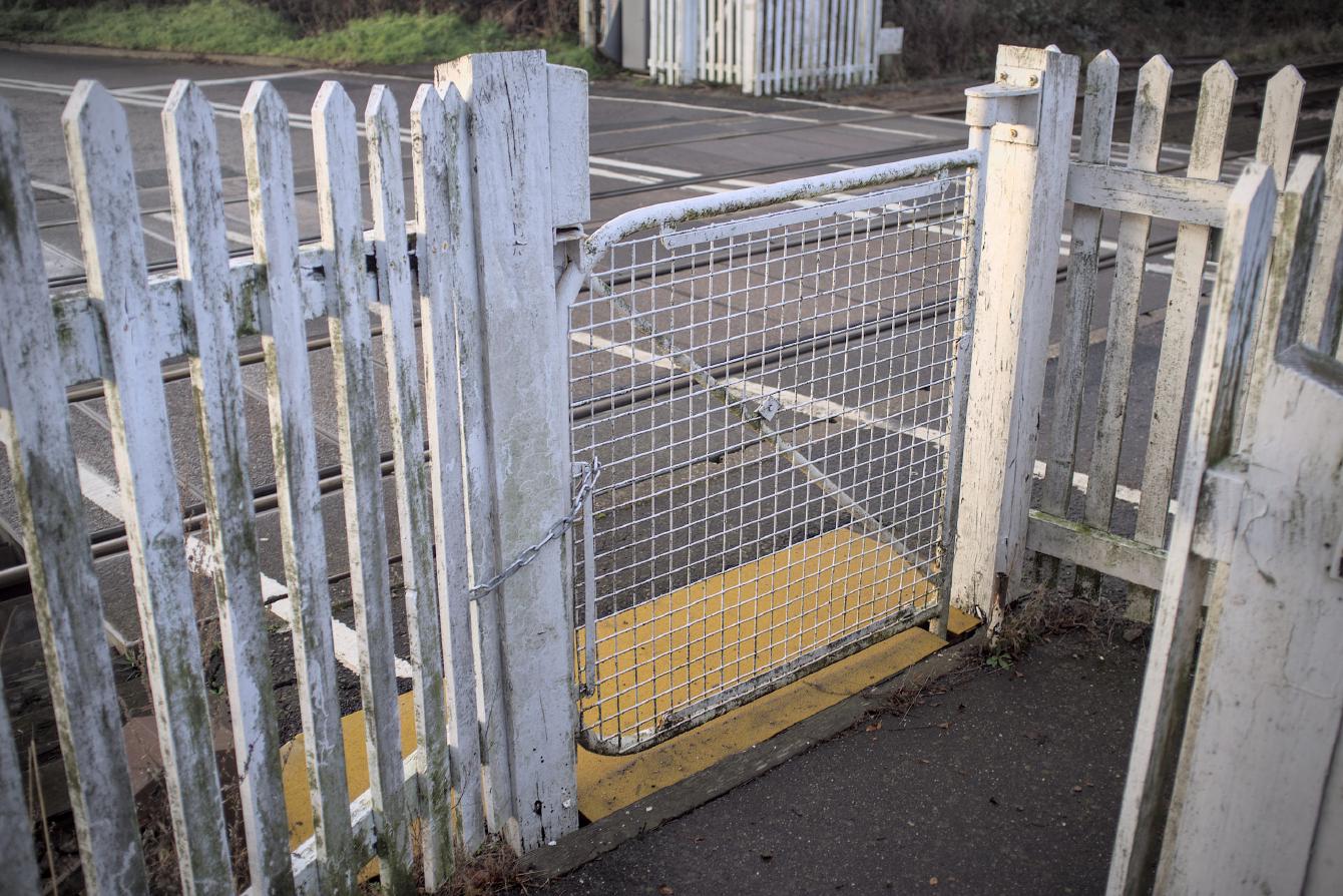 A white metal gate, chained shut, clearly of one-human width, leading on to a railway line.