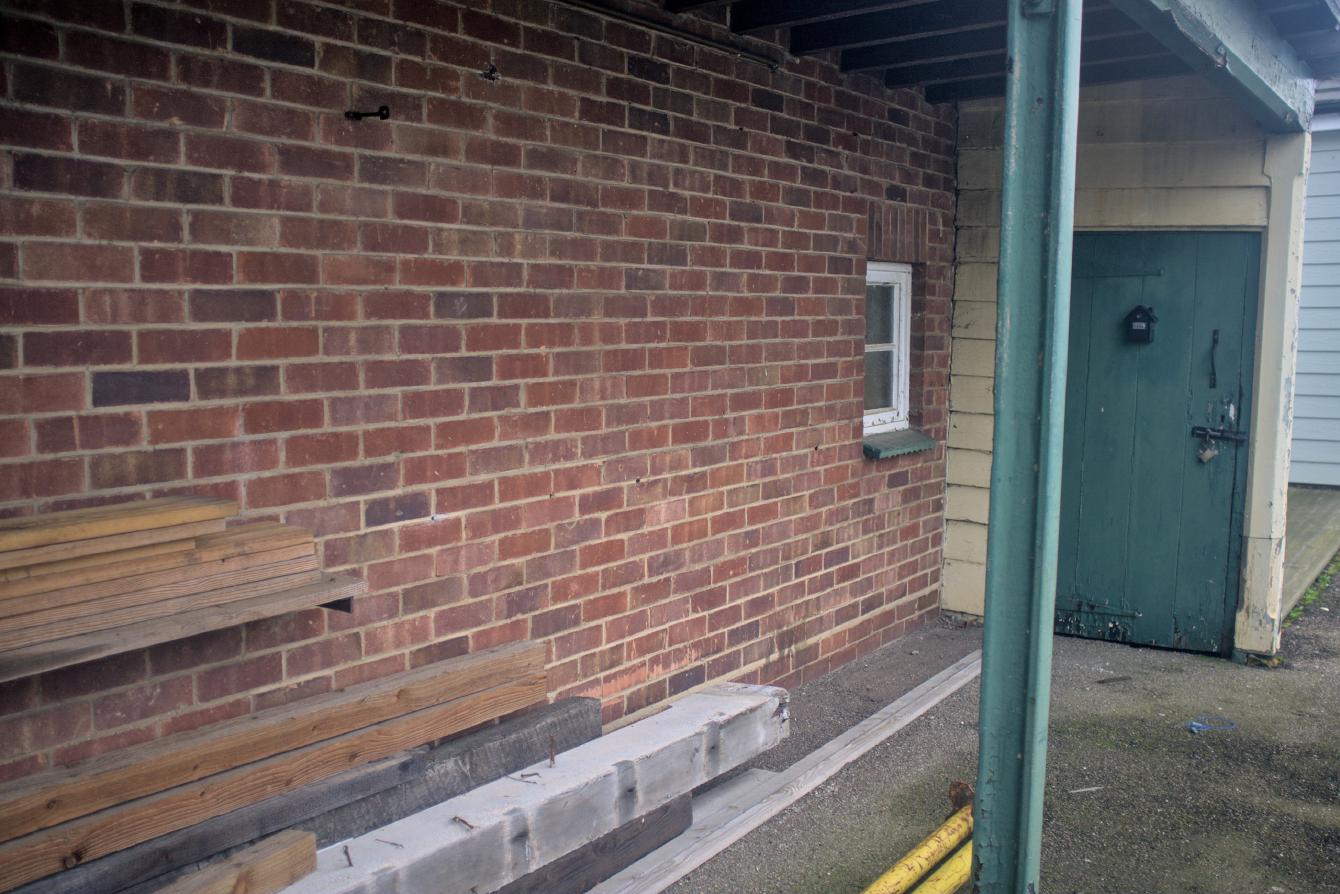 A small shelter with a wood canopy and a brick wall at the rear of it.