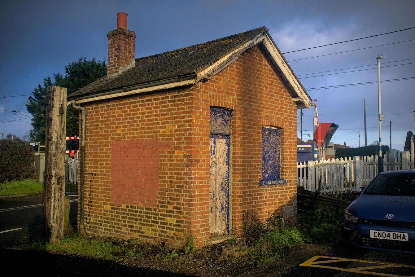 A small brick building, with an apex roof, a small entrance door, and one window covered by wooden board.