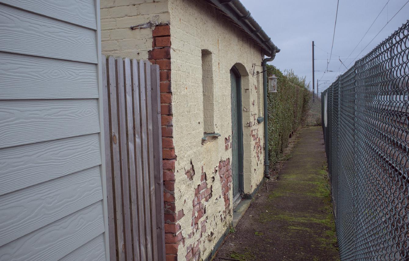 A store room; it is a brick-built building with some flaking cream paint.