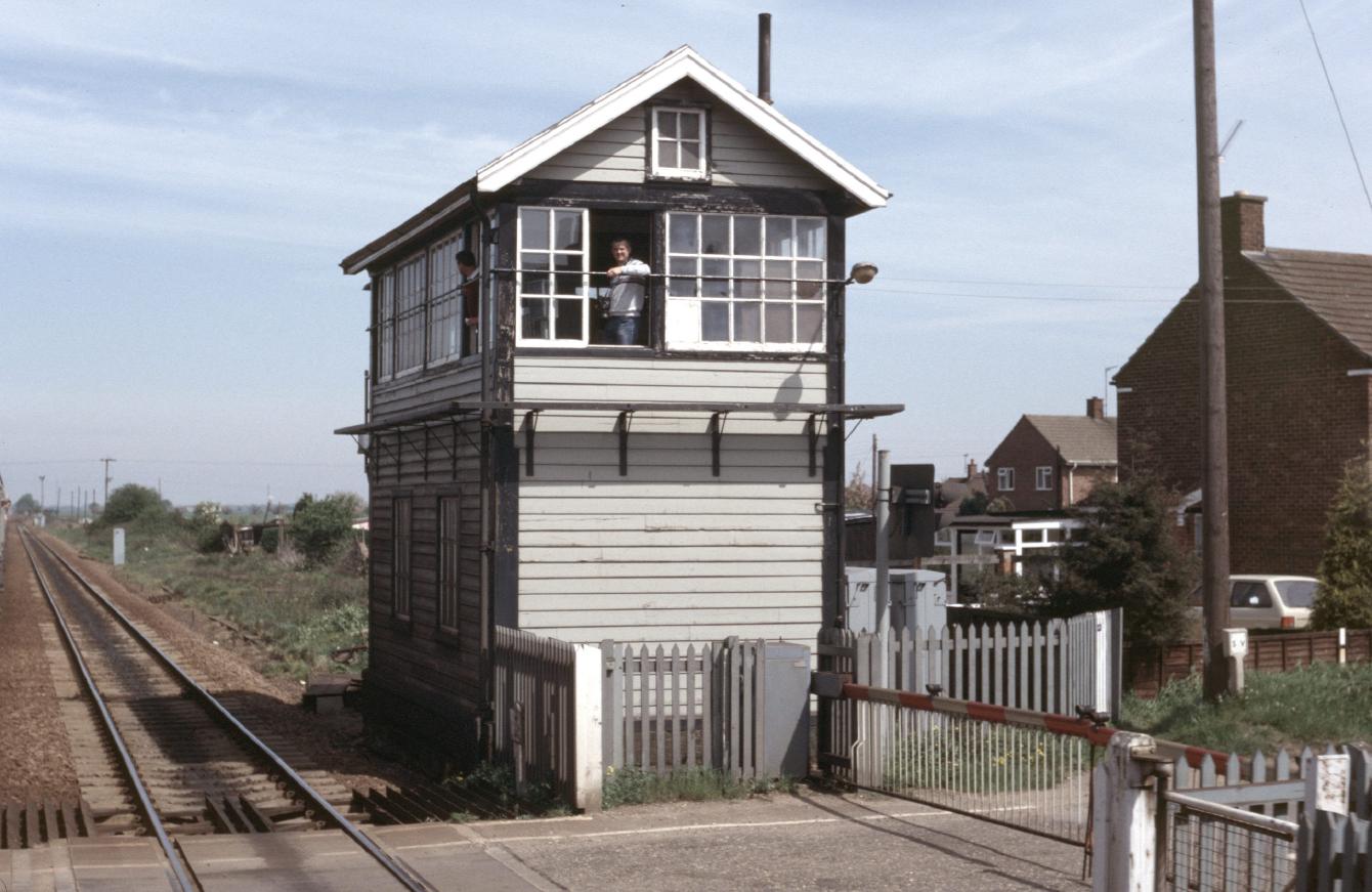 A photo of the Magdalen Road signal box painted white; a man with a camera on his neck looks out the window. A small balcony around two sides allows cleaning of the windows