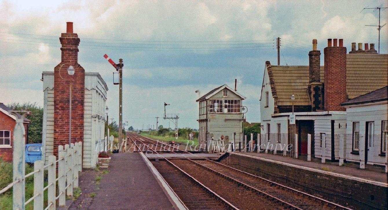 A white-painted wooden platform shelter, with a chimney; on the platform is a semaphore signal.