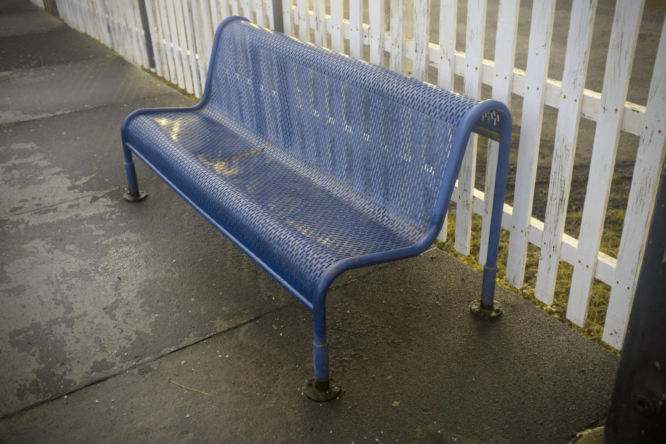 A steel bench; the ends are formed of bent tubing, while curved steel with a grate-like pattern forms the seating area.