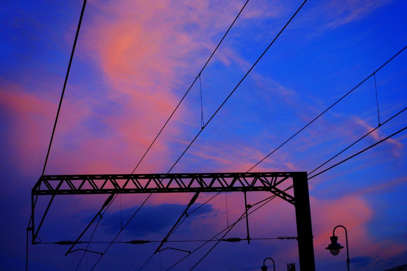 Against a purple sky, some 25kv overhead railway electrification wires and its mast draw black lines.