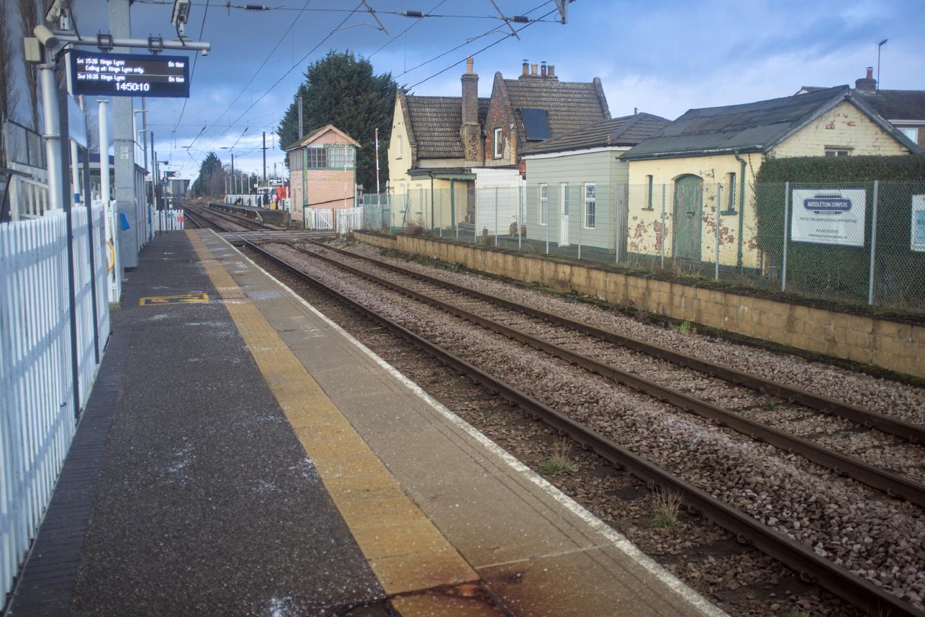 A look down platform 2 at Watlington, looking towards King&rsquo;s Lynn. Some disused station buildings and a platform are on the opposite side of the track. Overhead lines dominate the photo.
