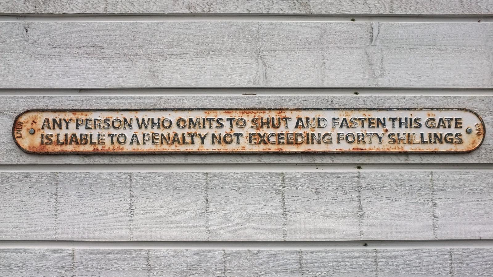 An LNER cast iron sign reading: Any person who omits to shut and fasten this gate is liable to a penalty not exceeding forty shillings.