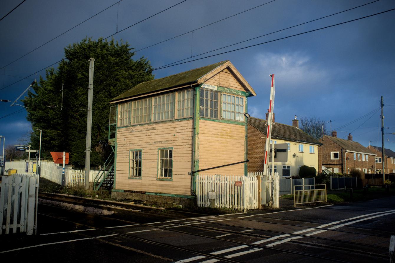 A green-and-cream two-storey signal box on a level crossing; the upper storey is glazed, and there are two windows in the bottom half.