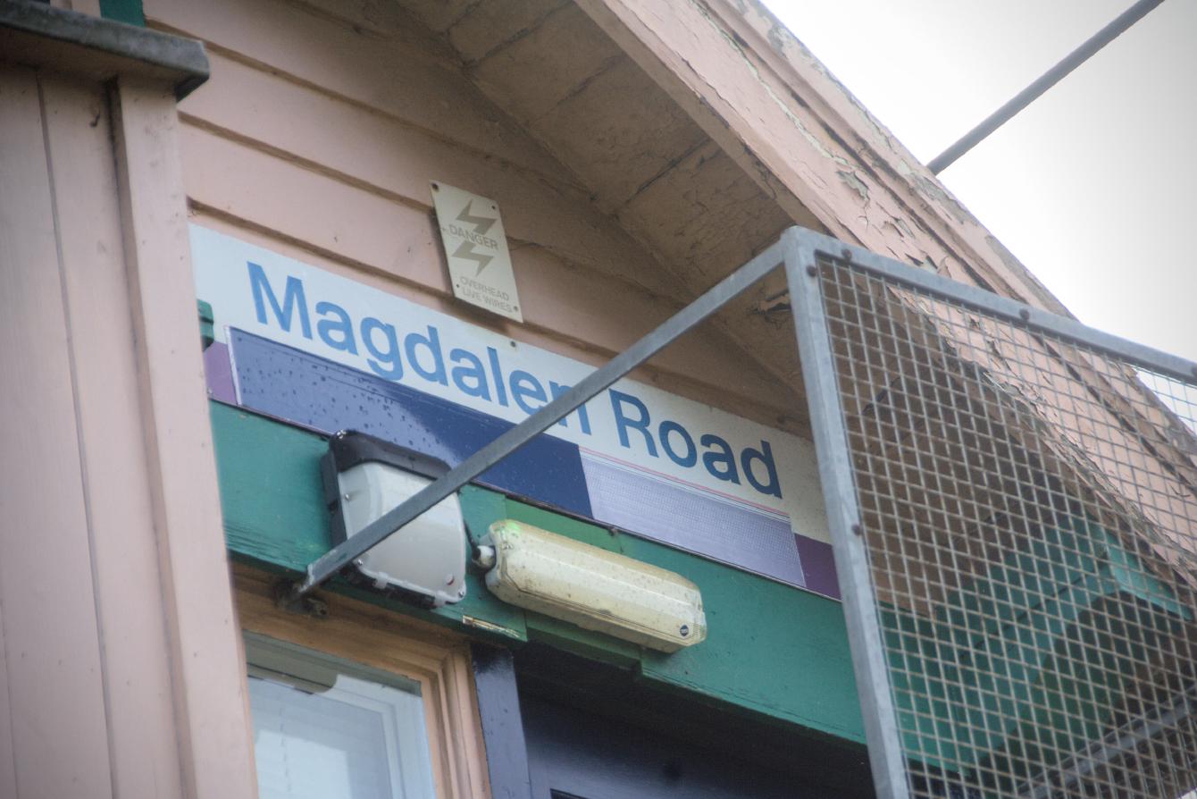 A Network SouthEast-era sign on a signalbox saying Magdalen Road, with some crude attempts at covering up the NSE &ldquo;flash&rdquo; branding.